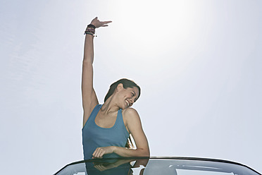 Spain, Majorca, Young woman with victory sign standing in cabriolet car - WESTF017101