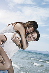 Spain, Majorca, Young man carrying woman on back at beach - WESTF017137