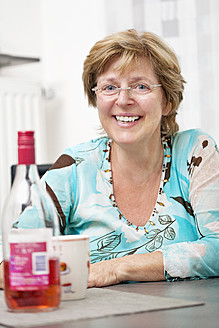 Mature woman sitting in kitchen, smiling, portrait - TSF000344