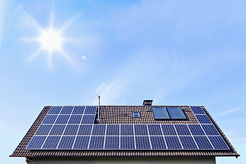 Germany, Solar panels on houseroof in front of blue sky with sun - TSF000345