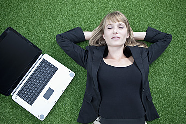 Deutschland, Bayern, München, Geschäftsfrau entspannt auf Rasen neben Laptop - MAEF003708