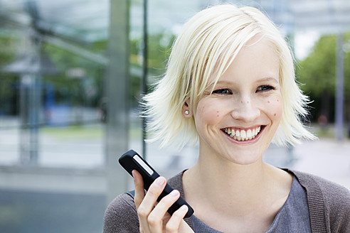 Deutschland, Bayern, München, Junge Frau mit Mobiltelefon, lächelnd - SPOF000038