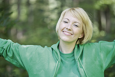 Germany, Bavaria, Schaeftlarn, Close up of young woman in forest with arms up, portrait, smiling - TCF001778