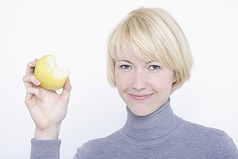 Nahaufnahme einer jungen Frau, die Obst vor weißem Hintergrund isst, Porträt, lächelnd - TCF001755