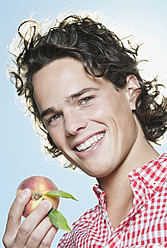 Italy, Tuscany, Close up of young man holding peach, smiling, portrait - PDF000189