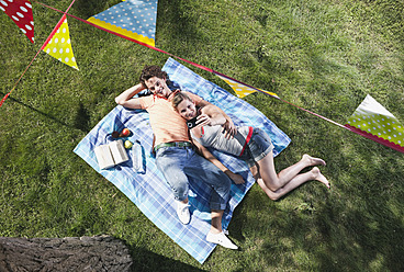 Italy, Tuscany, Young couple lying on picnic blanket with food and flag line hanging above - PDF000192