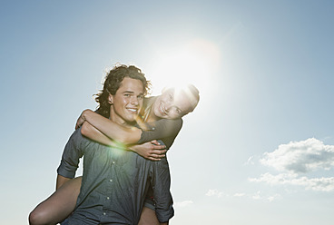 Italien, Toskana, Junger Mann trägt Frau auf seinem Rücken gegen die Sonne - PDF000212