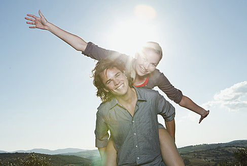 Italien, Toskana, Junger Mann trägt Frau auf seinem Rücken gegen die Sonne - PDF000215