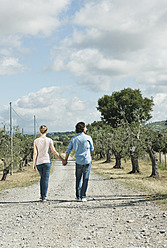Italien, Toskana, Junges Paar hält sich an den Händen und geht auf der Landstraße - PDF000265