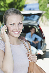 Italien, Toskana, Nahaufnahme einer jungen Frau, die mit einem Handy telefoniert und ein Auto mit Gepäck im Hintergrund - PDF000291