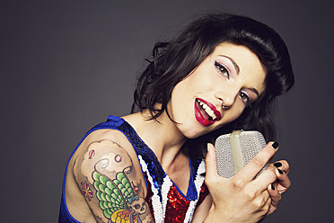 Close up of young woman with tattoo on her hand against grey background, singing, portrait - MBE000176
