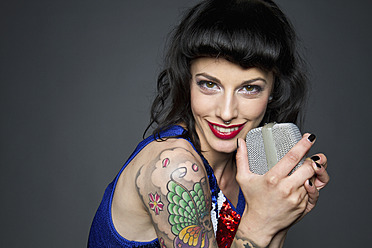 Close up of young woman with tattoo on her hand against grey background, singing, portrait - MBE000177