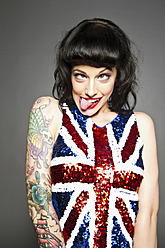 Young woman with tattoo on her hand making funny faces against grey background - MBE000185