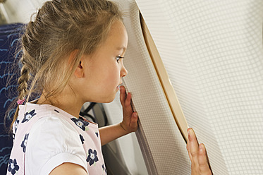 Germany, Munich, Bavaria, Girl looking through window in economy class airliner - WESTF017179