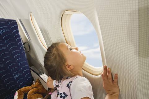 Germany, Munich, Bavaria, Girl looking through window in economy class airliner stock photo