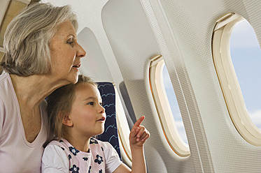 Germany, Munich, Bavaria, Senior woman and girl looking through window in economy class airliner - WESTF017187