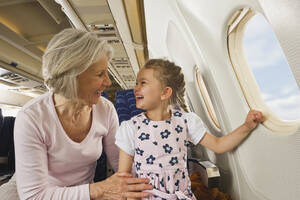 Deutschland, München, Bayern, Ältere Frau und Mädchen lächelnd neben dem Fenster in der Economy Class eines Flugzeugs - WESTF017188