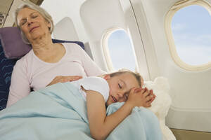 Deutschland, München, Bayern, Ältere Frau und Mädchen schlafen neben dem Fenster in der Economy Class eines Flugzeugs - WESTF017191