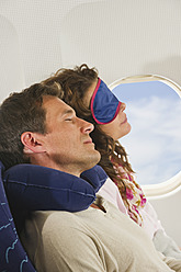 Deutschland, München, Bayern, Mittleres erwachsenes Paar, das eine Schlafmaske trägt und in der Economy Class eines Flugzeugs schläft - WESTF017207