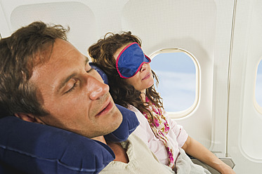 Deutschland, München, Bayern, Mittleres erwachsenes Paar, das eine Schlafmaske trägt und in der Economy Class eines Flugzeugs schläft - WESTF017208