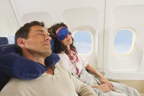 Deutschland, München, Bayern, Mittleres erwachsenes Paar, das eine Schlafmaske trägt und in der Economy Class eines Flugzeugs schläft, lizenzfreies Stockfoto