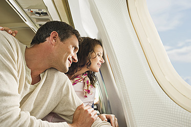 Deutschland, München, Bayern, Mittleres erwachsenes Paar schaut durch das Fenster in der Economy Class eines Flugzeugs - WESTF017213
