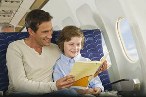 Deutschland, München, Bayern, Mann und Junge lesen ein Buch in der Economy Class eines Flugzeugs - WESTF017220