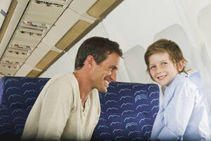Deutschland, München, Bayern, Mann und Junge lächelnd in der Economy Class eines Flugzeugs - WESTF017224