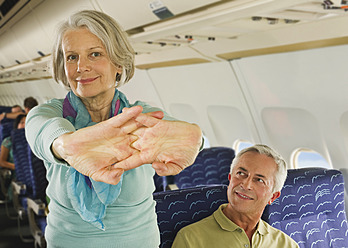 Germany, Munich, Bavaria, Senior woman stretching and man looking in economy class airliner - WESTF017233