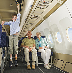 Deutschland, München, Bayern, springender Junge mit Kapitänsmütze und ältere Menschen in der Economy Class eines Flugzeugs - WESTF017240