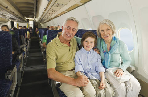 Deutschland, München, Bayern, Junge sitzt neben älteren Menschen in der Economy Class eines Flugzeugs, lizenzfreies Stockfoto