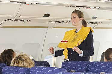Germany, Munich, Bavaria, Stewardess guiding passengers with life vest in economy class airliner - WESTF017256