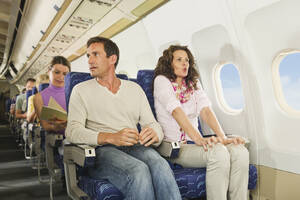 Deutschland, München, Bayern, Passagiere lesen ein Buch in der Economy Class eines Flugzeugs - WESTF017260