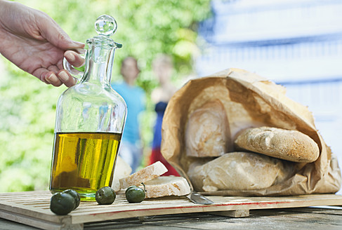 Italien, Toskana, Magliano, Nahaufnahme von Brot, Olivenöl und Oliven auf Holztisch - WESTF017277