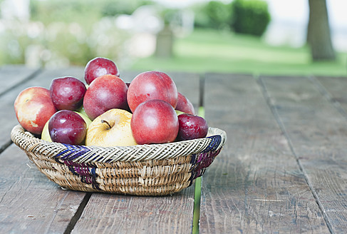Italien, Toskana, Magliano, Obstkorb mit Äpfeln und Pflaumen auf Holztisch - WESTF017345
