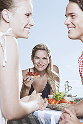 Italien, Toskana, Magliano, Junge Frau hält Essen und Freunde im Vordergrund, lächelnd - WESTF017383