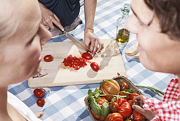 Italien, Toskana, Magliano, Junge Frau schneidet Tomaten am Tisch mit Freunden im Vordergrund - WESTF017387