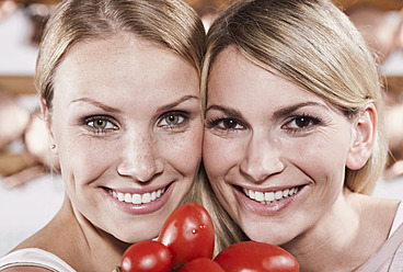 Italien, Toskana, Magliano, Nahaufnahme von zwei jungen Frauen mit Tomaten in der Küche, lächelnd, Porträt - WESTF017396
