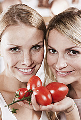 Italien, Toskana, Magliano, Nahaufnahme von zwei jungen Frauen mit Tomaten in der Küche, lächelnd, Porträt - WESTF017397