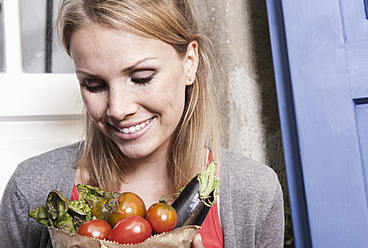 Italy, Tuscany, Magliano, Close up of young woman holding bag of vegetables, smiling - WESTF017403