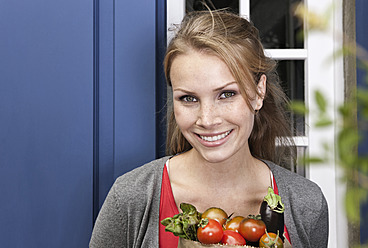 Italy, Tuscany, Magliano, Young woman holding bag of vegetables, smiling, portrait - WESTF017405