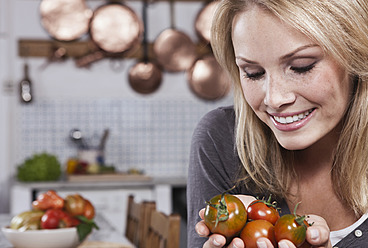 Italien, Toskana, Magliano, Junge Frau hält Tomaten in der Küche, lächelnd - WESTF017418
