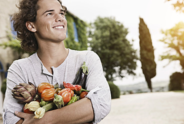 Italien, Toskana, Magliano, Junger Mann hält verschiedene Gemüsesorten, lächelnd - WESTF017440