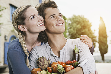 Italien, Toskana, Magliano, Junger Mann und Frau halten verschiedene Gemüsesorten, lächelnd - WESTF017448