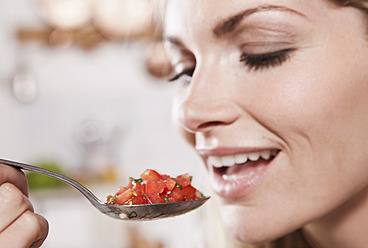 Italy, Tuscany, Magliano, Young woman eating spoon of chopped tomatoes, smiling - WESTF017460