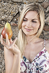 Italy, Tuscany, Magliano, Close up of young woman holding pear, smiling - WESTF017469