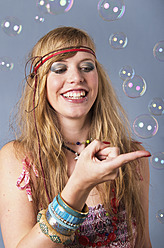 Junge Hippie-Frau mit Blasen vor grauem Hintergrund, lächelnd - MUF001091