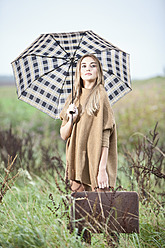 Germany, Bavaria, Young woman with umbrella carrying briefcase in grass - MAEF003799