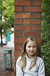 Germany, Berlin, Girl sitting in front of red brick wall - WESTF017471