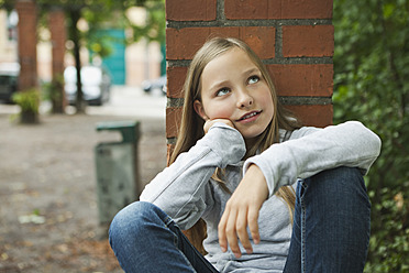 Germany, Berlin, Girl sitting in front of red brick wall - WESTF017472